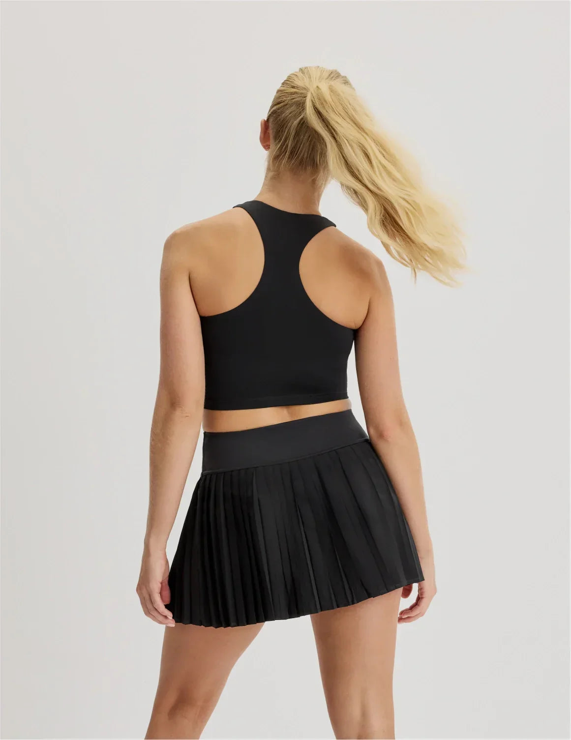 Back view of model wearing the Teen First Serve Pleated Skort highlighting the coverage and fit – Black – view 4 of 11